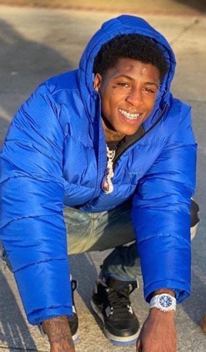 A Young Man In A Blue Jacket Crouches Down On His Skateboard And Smiles