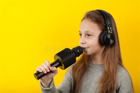 niña canta en un micrófono con un fondo amarillo karaoke para los niños foto de archivo imagen