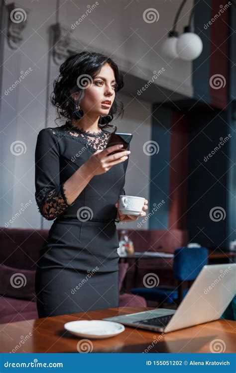 Beautiful Young Businesswoman In Cafe Using Mobile Phone And Drinking
