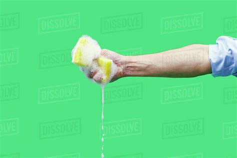 Hand Squeezing Soapy Sponge With Water Dripping On Green Background