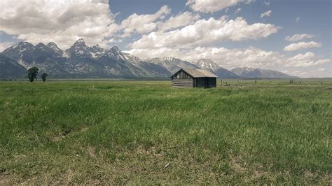 Beautiful Landscape With Grassland And Mountains With Cabin Under Sky