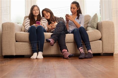Teenage Girls Sitting On Sofa Looking At Phones Stock Photo Dissolve