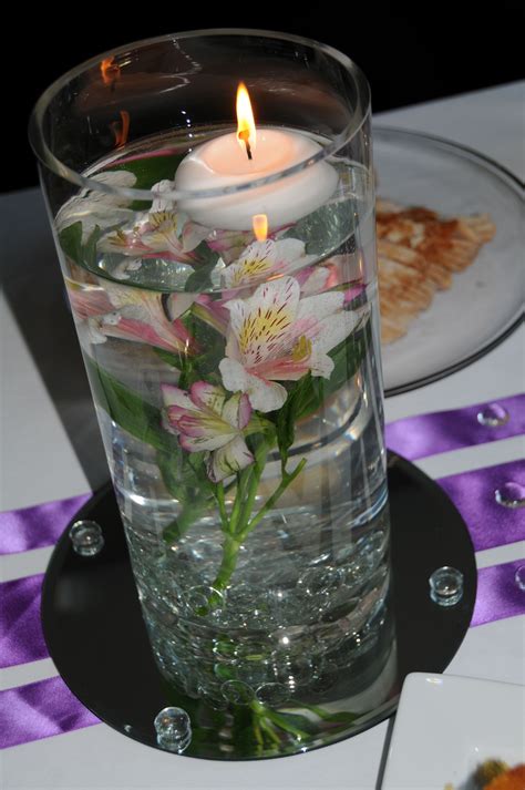 A Candle Is Lit In A Glass Vase With Water And Flowers On The Table Top