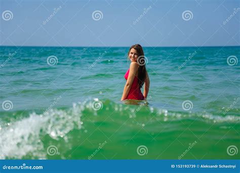 Young Long Haired Brunette In Red Beach Dress Standing Waist Deep In Turquoise Ocean Water On