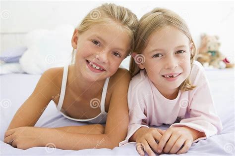 Twee Jonge Meisjes In Hun Pyjamas Die Op Een Bed Liggen Stock