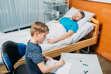 Son Drawing Pictures While Sick Father Laying On Hospital Bed At Ward