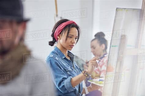 Focused Female Artist Painting At Easel In Art Class Studio Stock