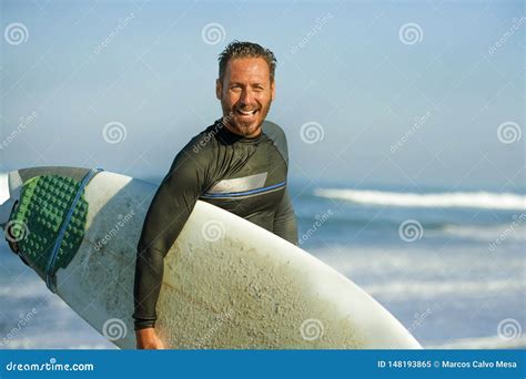 Handsome And Attractive Surfer Man In Neoprene Swimsuit Carrying Surf