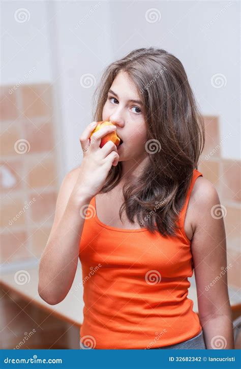 Девочка подросток в оранжевой футболке есть персик Стоковое Фото изображение насчитывающей