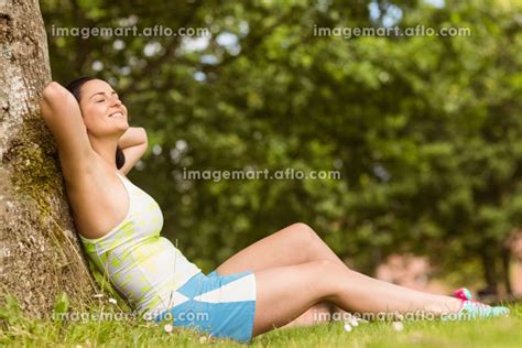 Smiling Fit Brunette Sitting And Relaxing Against A Treeの写真素材 110024275 イメージマート