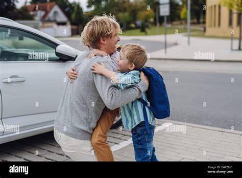 Father saying goodbye to sons in front of school building, hugging them