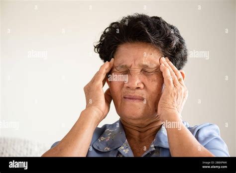 Asian Old Woman Sitting On Sofa And Having A Headache At Home Senior Healthcare Concept Stock