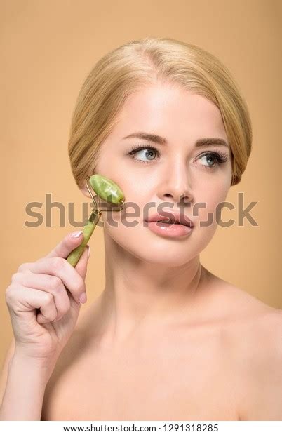 Attractive Naked Girl Massaging Face With Jade Roller And Looking Away