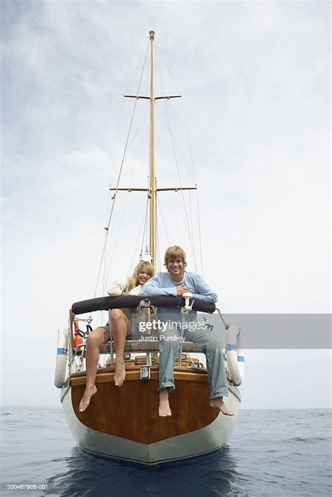 Young Couple Sitting At Back Of Sailboat Smiling Portrait High Res
