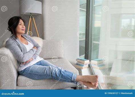 Mature Asian Woman Relaxing At Home Sitting On Sofa Chair Enjoying View