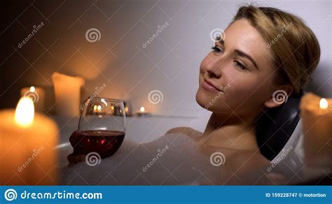 Attractive Woman Lying In Bath With Foam Bubbles And Candles Drinking