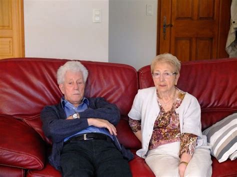 an older man and woman sitting on a red couch