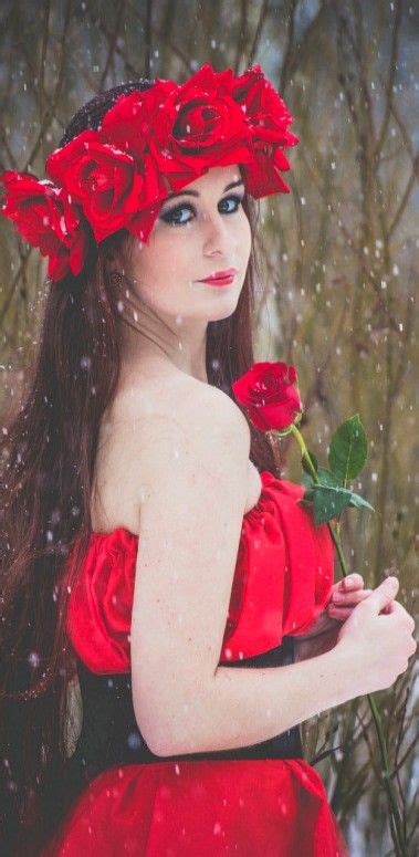 a woman in a red dress holding a rose and looking at the camera with snow falling on her