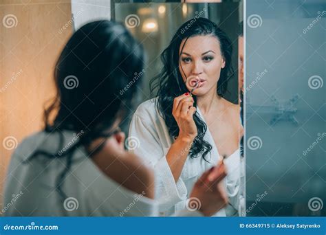 Young Beautiful Woman Brunette In The Bathroom And White Bathrobe Making Make Up Near Mirror