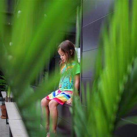 Thoughtful Girl Looking Down While Sitting On Window Sill Seen Through Plants Photograph By