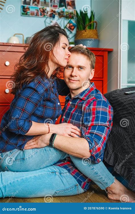 Beautiful Young Couple In Jeans Hugging And Smiling Sitting In Bedroom With Red Wardrobe In