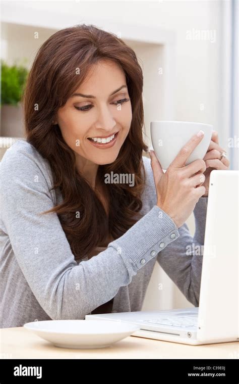 Beautiful Brunette Woman At Home Sitting At A Table Using Her Laptop Computer Smiling And
