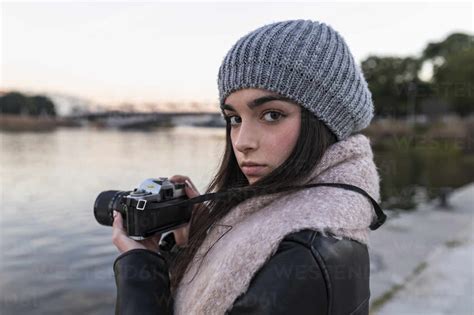 Beautiful Teenage Girl Holding Camera By River During Sunset Stock Photo