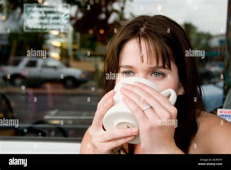 A Young Woman Sips Her Coffee And Talks On The Phone As She Relaxes In