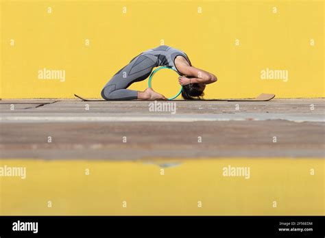 Flexible Woman With Yoga Wheel Bending Over Backwards By Yellow Wall