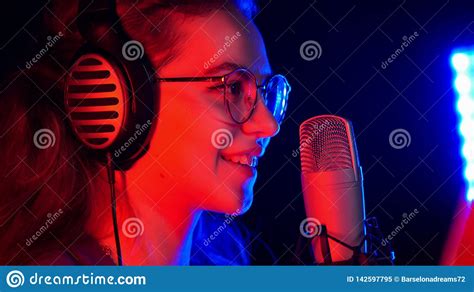 A Young Smiling Woman In Glasses Singing By The Microphone In Neon