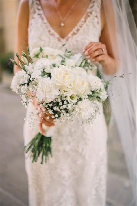a woman in a wedding dress holding a bridal bouquet with white flowers and greenery