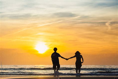 Silhouettes Of Man And Woman Holding Hands On The Beach At Sunset