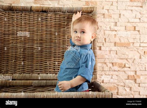 Stylish Baby Boy In Denim Shirt In A Wicker Basket On A Stone Wall