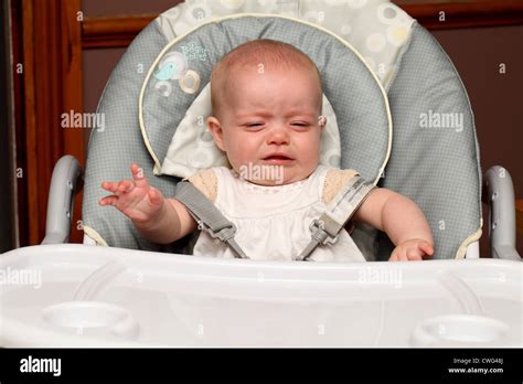 A 6 month old baby girl, sitting in a high chair, cries while waiting