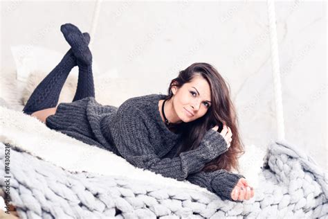 Beautiful Sexy Tan Brunette Woman Posing In Bedroom Wearing Cozy Grey Sweater And Knitted Socks