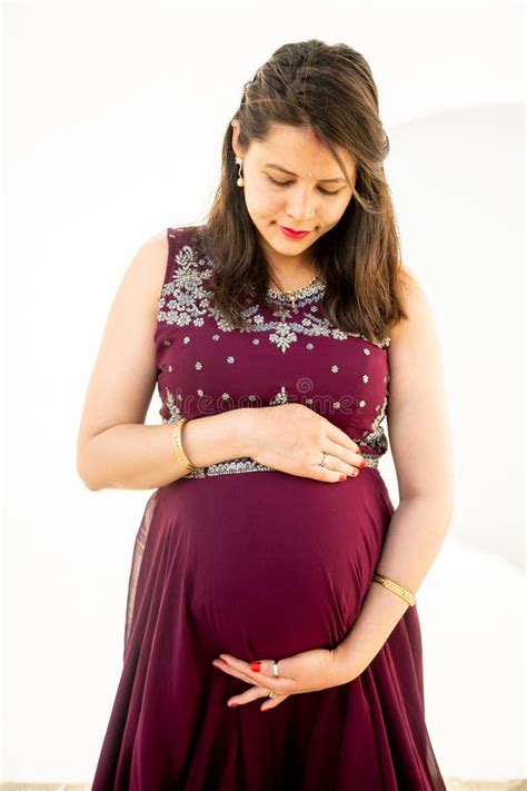 Young Asian Indian Pregnant Woman Looking At Belly Standing Against