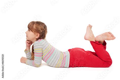 Side View Of Smiling Child Girl Lying On Stomach On The Floor With