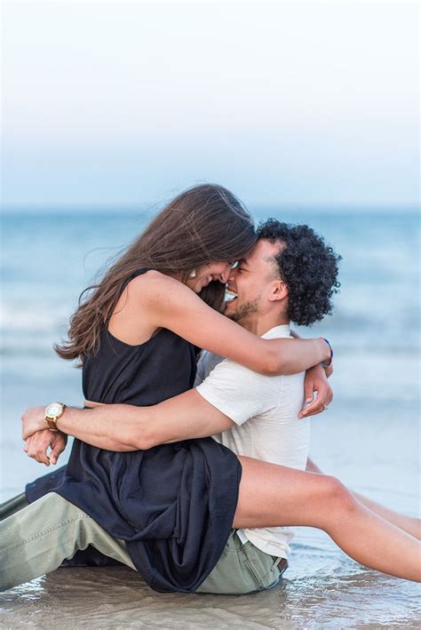 A Man And Woman Are Sitting On The Beach Hugging Each Other As They Kiss In Front Of The Ocean