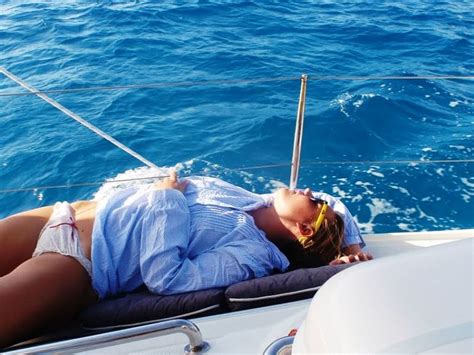 A Woman Laying Down On The Back Of A Boat In The Blue Water With Her Eyes Closed