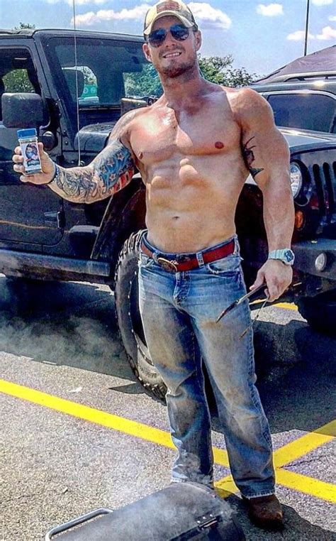 A Shirtless Man Standing In Front Of A Truck Holding A Cell Phone And