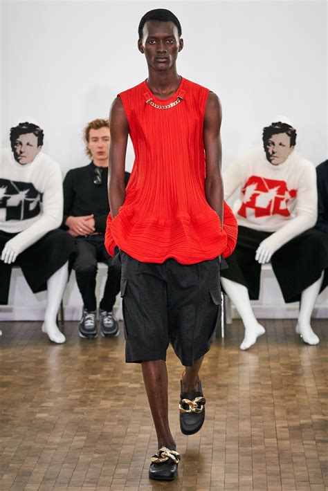 A Model Walks Down The Runway In An Orange Top And Black Shorts