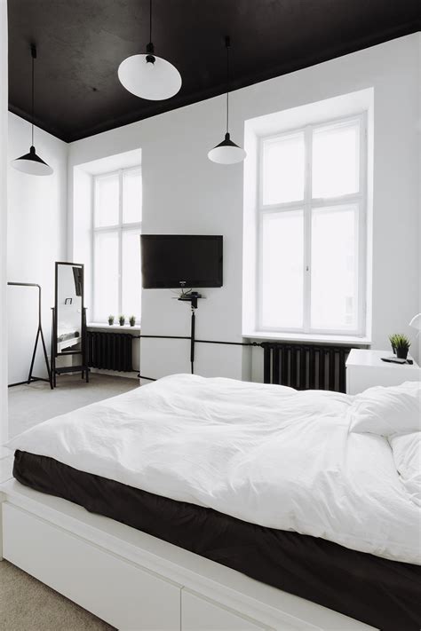 An elegant contemporary bedroom with a white upholstered bed, white nightstands, a chic chandelier and an artwork. Industrial Style Apartment with Meeting Room