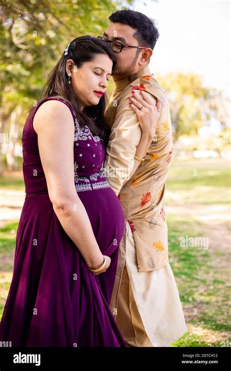 Young Asian Indian Pregnant Woman With Her Husband Wearing Traditional Outfit Standing In Park