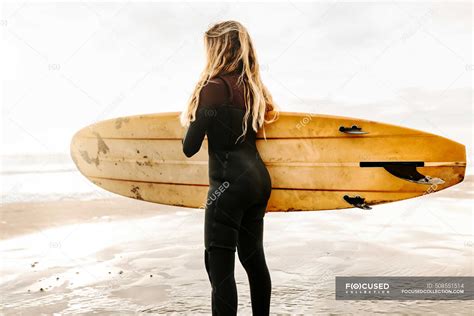 Vista Lateral De La Mujer Surfista Vestida Con Traje De Neopreno De Pie Mirando Hacia Otro Lado