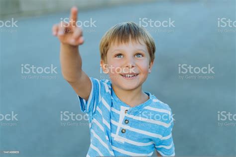 Portrait Of Little Cheerful Caucasian Boy Pointing Upwards To The Sky