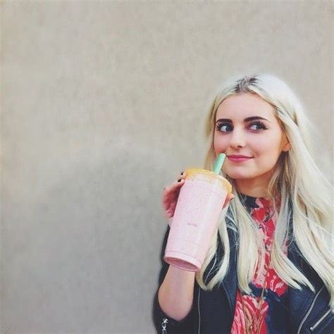 A Blonde Woman Holding A Pink Drink And Looking At The Camera