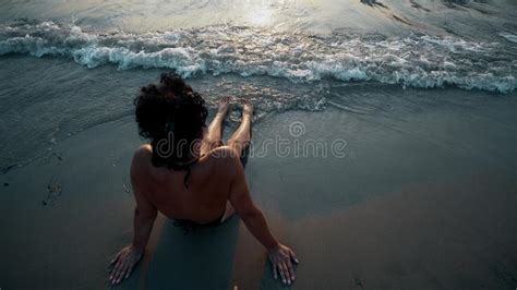Woman Legs And Bare Feet Sitting On Golden Sand Beach At Sunset Stock