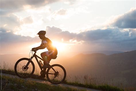 man riding a bike uphill against sunset sky by stocksy contributor ibex media stocksy