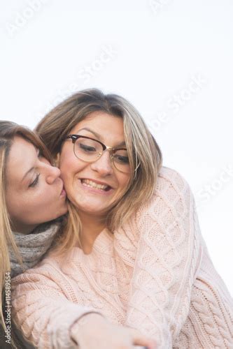 Portrait Of Two Simpering Young Girls Kissing Each Other Outdoors