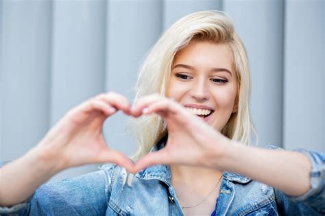 Premium Photo Charming Blonde Woman Making Heart Sign With Her Fingers At The Shutters Background